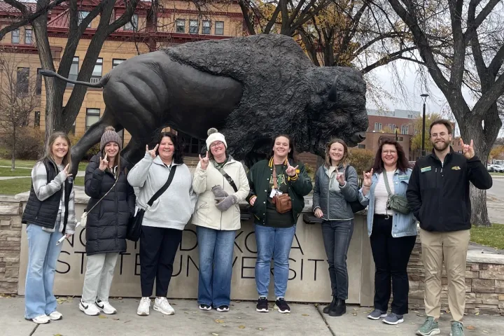 Local educators pose in front of the Bison statue on campus.