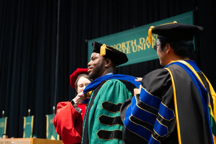 graduate receiving his commencement regalia during the ceremony