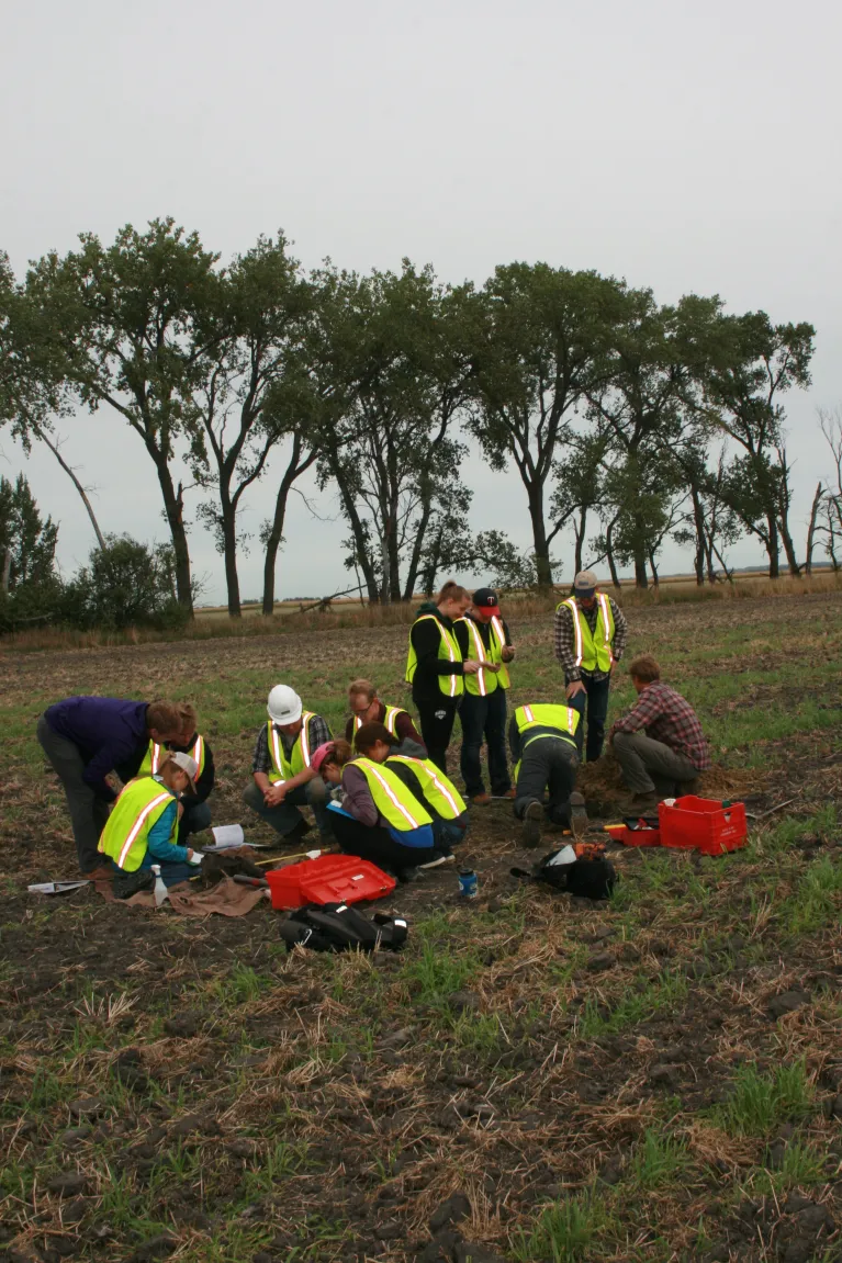 A group of ten people in high visibility vests examining the soil in a field