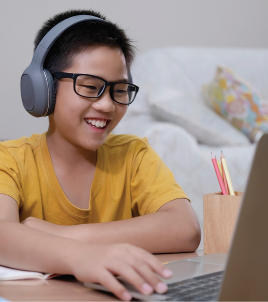 Young boy in glasses wearing headphones and working on computer