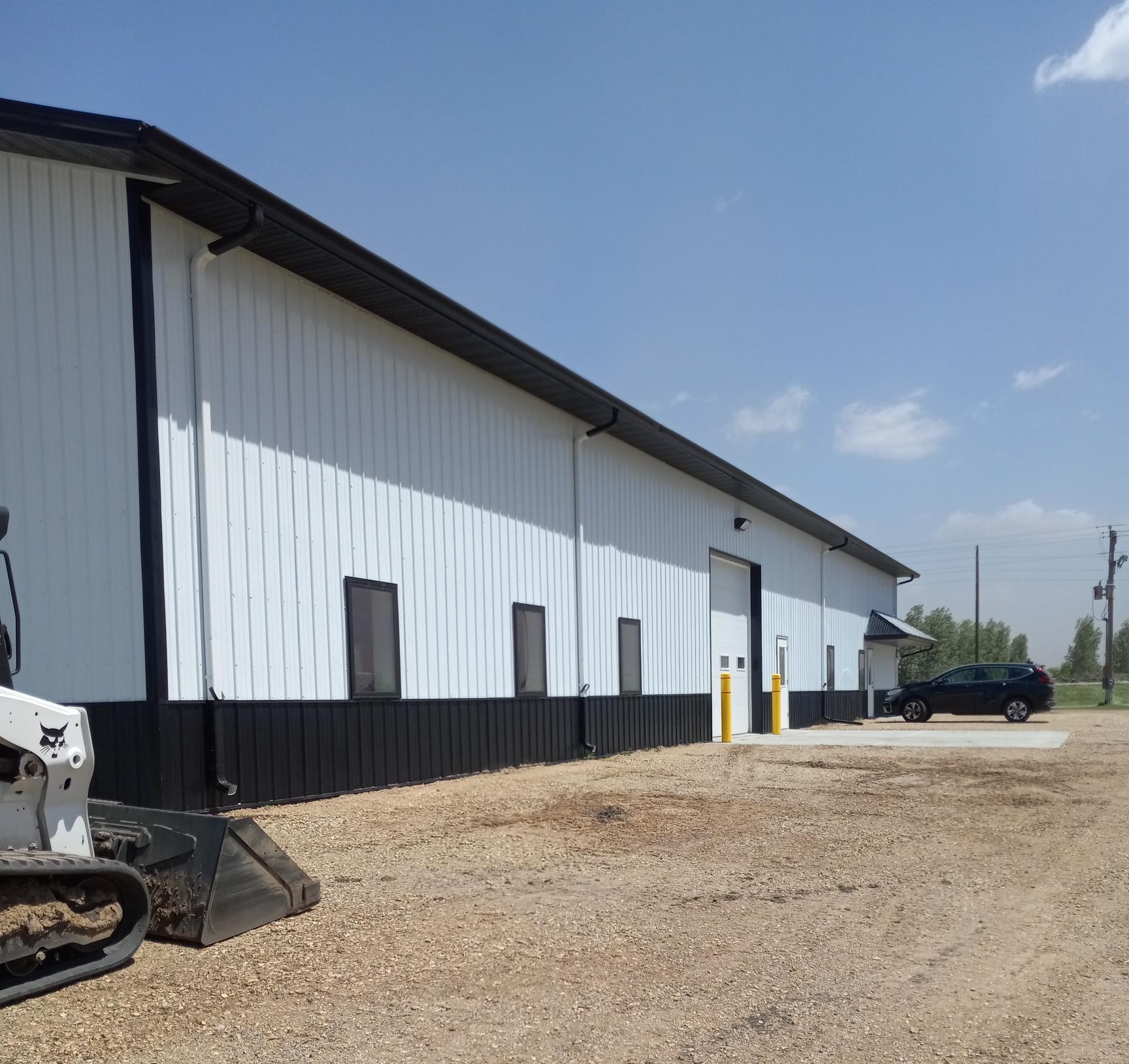 A white steel building with a black roof and wainscoting.