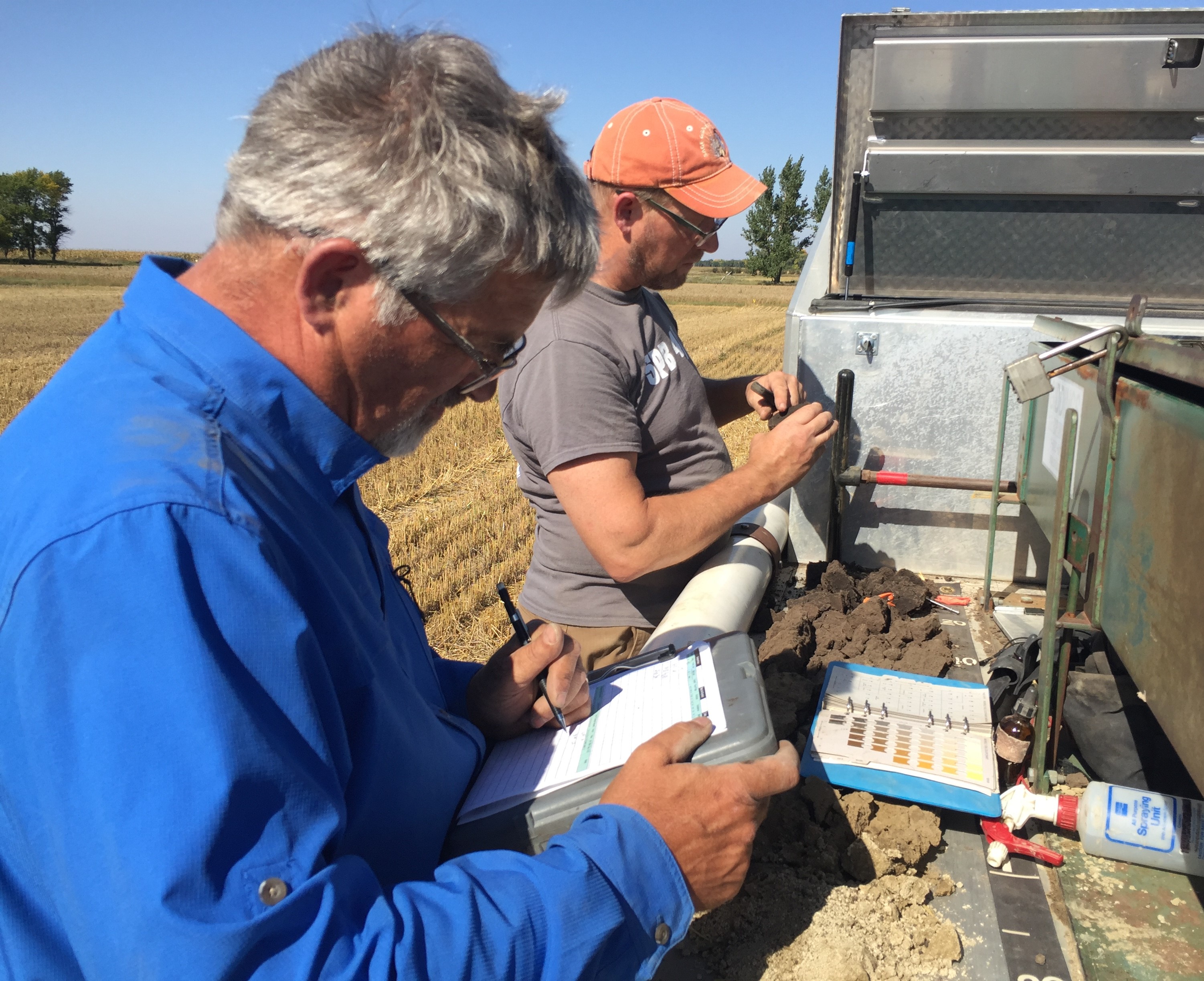 Two people are outside, grading comparing soils to guides from the back of their pickup. 