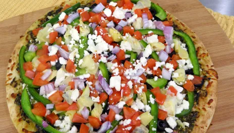 photograph of pesto pizza on a wooden cutting board