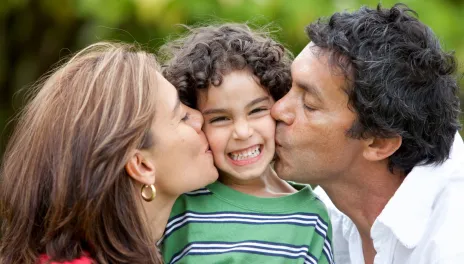 mother and father kissing son on each cheek