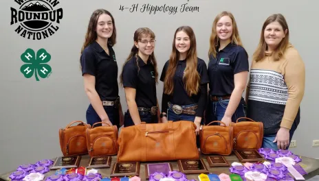 Five women stand behind table displaying awards and ribbons. 