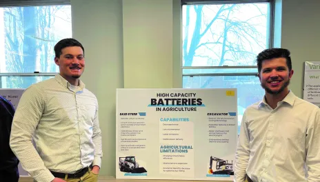 Two people in white shirts stand next to research poster sitting on a table. 