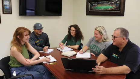 five people sitting around a table in a meeting 