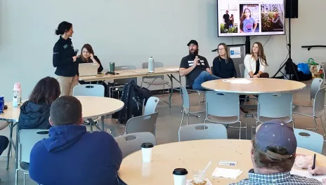 Two women presenting to several tables of attendees