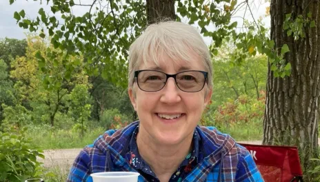 Kathy is sitting at a picnic table with food and some Aronia berry wine.