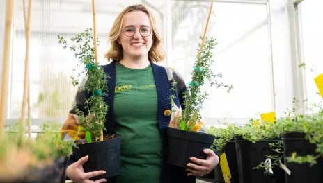 A woman holds two plants in a garden nursery