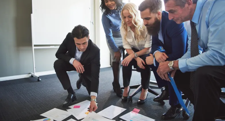 Group of people looking at papers scattered on conference room floor