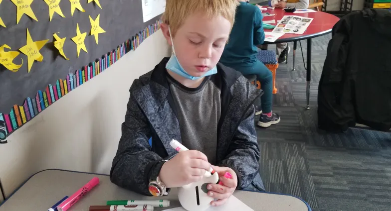 boy decorating piggy bank with markers