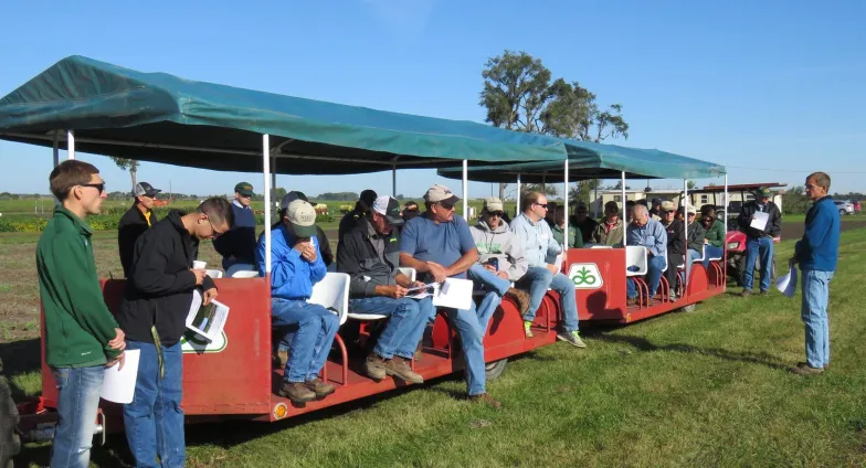 About 30 people riding on two red trailers with seats and green canopies at the 2017 Oakes Irrigation Site Field Day.