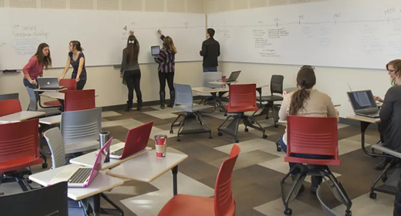 Students collaborating together during class lecture. Utilizing whiteboards and their computers to create a timeline.