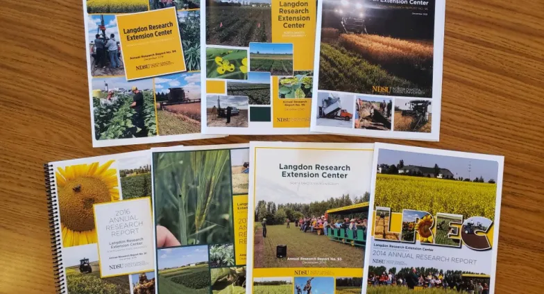 Six booklets with full color photos on the front are displayed on a wooden table.