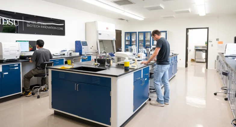 Photo of the level two lab. Two researchers are working at different lab benches and there are various scientific equipment set up around the room.