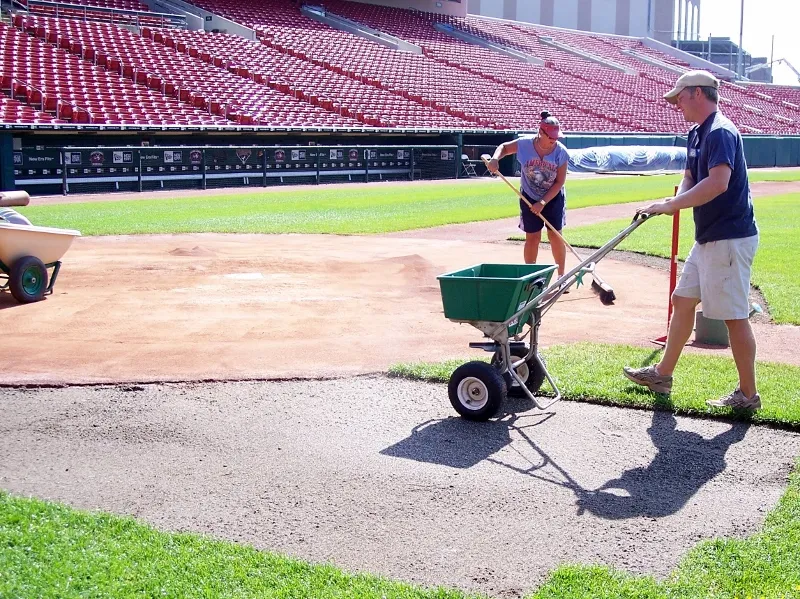 two people fertilizing turf at baseball field