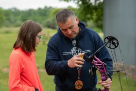 Man helps girl with a archery boy