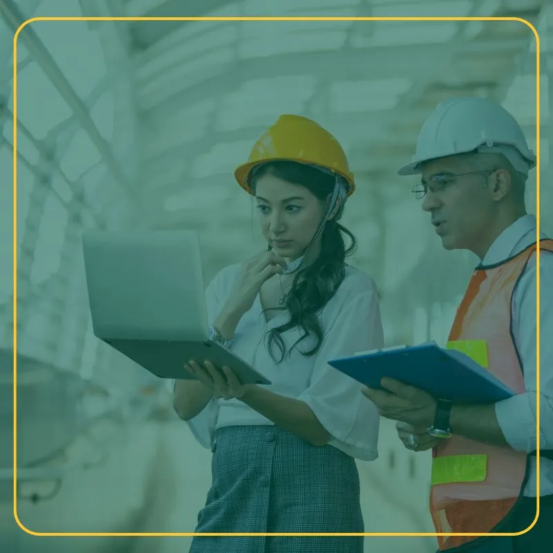 two Engineers in hard hats looking at plans on a laptop