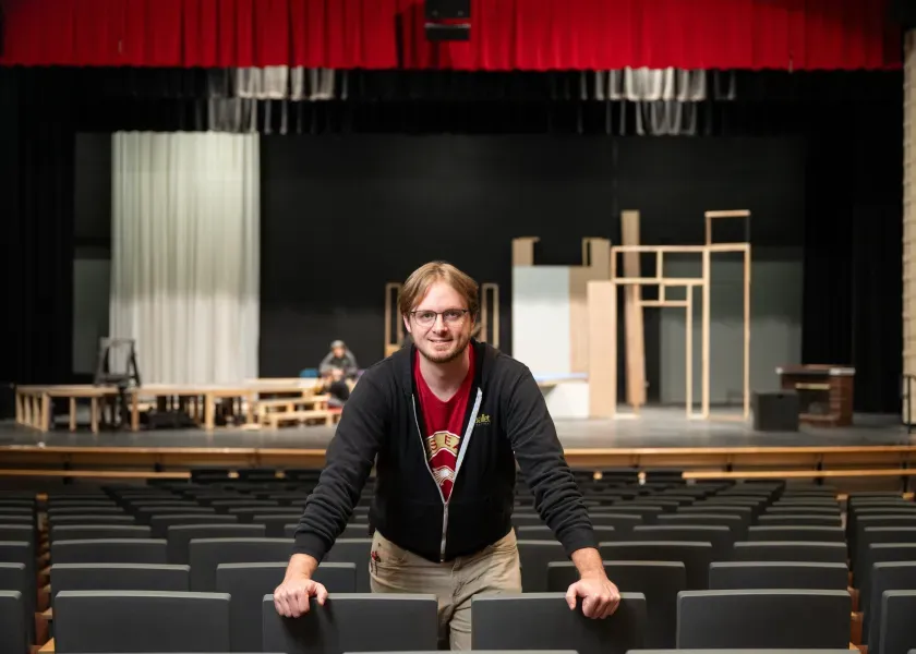 Mr. Lynch standing in theater seats with stage in background while smiling at the camera.