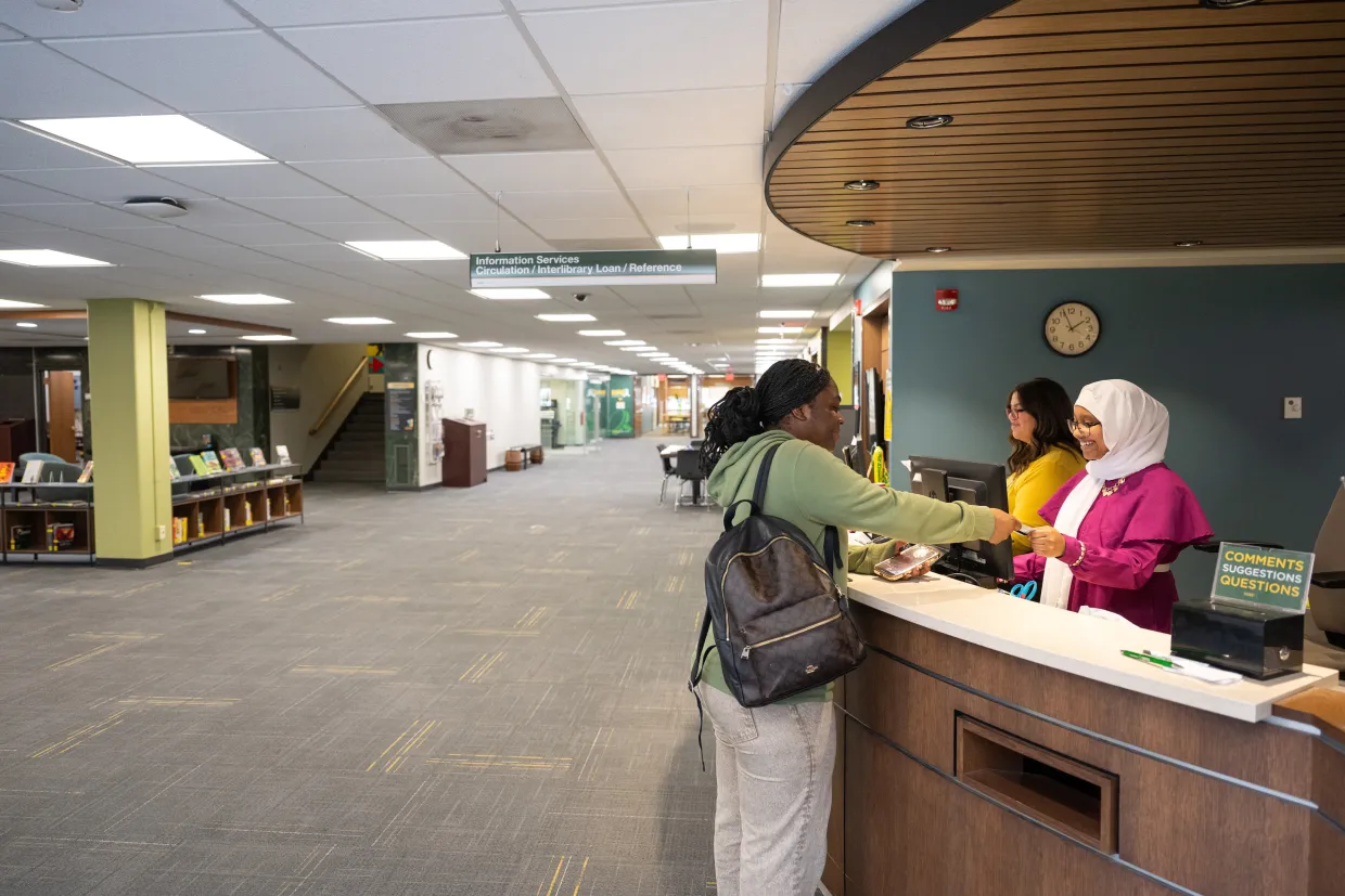 A student stands at the front desk of the NDSU Main Library.