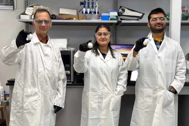 A professor and two students dressed in lab coats in a lab, each holding chicken eggs